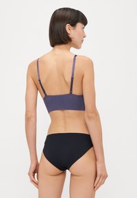 Bralette viola con un motivo texturizzato, spalline regolabili; abbinato a slip bikini neri a vita alta, tessuto liscio, design minimalista.