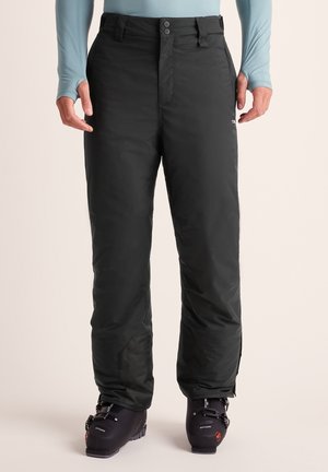 Black insulated snow pants worn over ski boots, shown on a person from waist to feet wearing a light blue long-sleeve top.