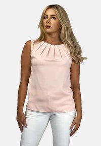 Bezramienna bluzka w odcieniu różu z plisowanym dekoltem, gładką teksturą i delikatnym połyskiem; zestawiona z białymi spodniami.