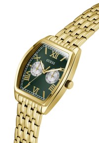 Gold-tone square watch with green dial, Roman numerals, two subdials, and a woven metal bracelet. Features a push crown and contrasting accents.