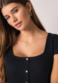 Sötétkék bordázott felsőrész, négyzet alakú nyakkivágással és öt fehér gombbal az elején. Rövid ujjú és testhezálló kialakítású.