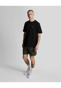 Black short-sleeve t-shirt with yellow logo; olive green shorts; white sneakers; textured fabric; relaxed fit; ankle socks.