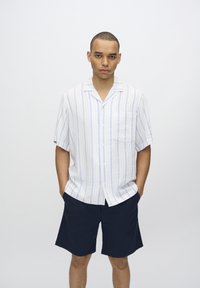 Koszula typu short-sleeve w jasnoniebieskie i białe paski z kieszeni�ą, w połączeniu z ciemnoniebieskimi szortami. Gładki materiał i luźny krój.