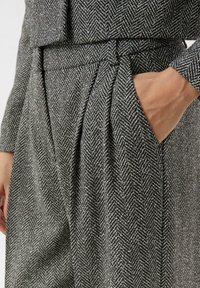 Szare spodnie w jodełkę z wysokim stanem, plisą i bocznymi kieszeniami. Tkanina ma teksturowany splot, który dodaje głębi.