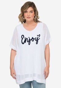 Top oversize de malla blanca con escote en forma de V. Presenta la palabra "Enjoy" en letras marinas, mangas cortas y un corte holgado. Textura suave, diseño casual.