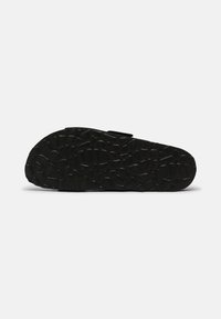 Chaussures noires avec une semelle en caoutchouc texturé à motif géométrique. Le design de la chaussure comprend une partie supérieure lisse et une sangle sur le côté.