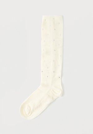 Hvid knæstrømpe med små sølvfarvede rhinsten udsprinklet over stoffet.