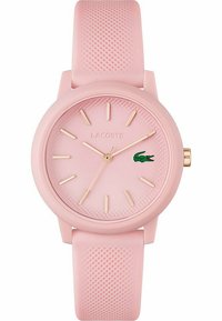 Montre ronde en silicone rose avec un bracelet texturé, des marqueurs d'heures dorés et un logo de crocodile vert. Design minimaliste avec une finition douce.