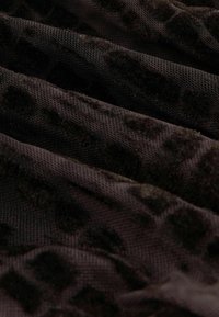 Gros plan d'un tissu texturé brun foncé avec un motif léopard velouté en relief et un tissage tricot visible.