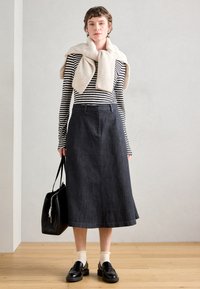 Σατέν φούστα μέχρι τους αστραγάλους σε σκούρο μπλε, συνδυασμένη με ένα μαύρο και λευκό ριγέ μπλουζάκι με μακριά μανίκια. Συμπληρωμένη με ένα ελαφρύ κρεμ πουλόβερ και μαύρη τσάντα.