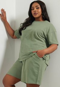 Olivgrön bomulls t-shirt och shorts-set med avslappnad passform, korta ärmar och sidfickor. Slät textur och minimal design.