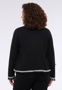 Černý pletený kabát s třásněmi na spodním lemu a stříbrným akcentem, s kulatým výstřihem a dlouhými rukávy, zobrazený zezadu. Měkká textura.