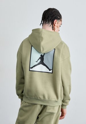 Hanorac cu glugă de culoare verde oliv, având un mare logo Air Jordan, de culoare neagră, într-un pătrat de culoare albastru deschis pe spate. Material moale, texturat.
