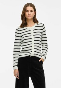 Stickad cardigan med horisontella svartvita ränder, med rund halsringning, knappstängning och ribbade ärmslut. Slät textur.