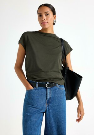 Olivengrøn kortærmet skjorte, afslappet pasform, parret med højtaljede blå denim jeans og et sort bælte; accessoriseret med en sort tote bag.