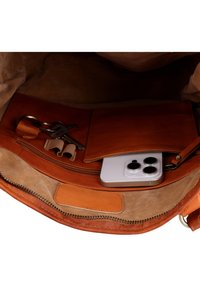 Brown leather bag interior with set of keys on a ring and a silver smartphone with triple camera lenses.