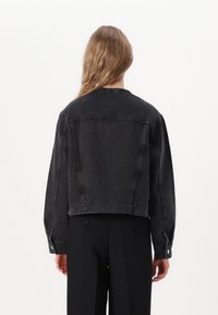Črna jeans jakna s skrajšanim dizajnom, vidnimi šivi in gumba na manšetah, z enostavno hrbtno stranjo in sproščenim krojem.