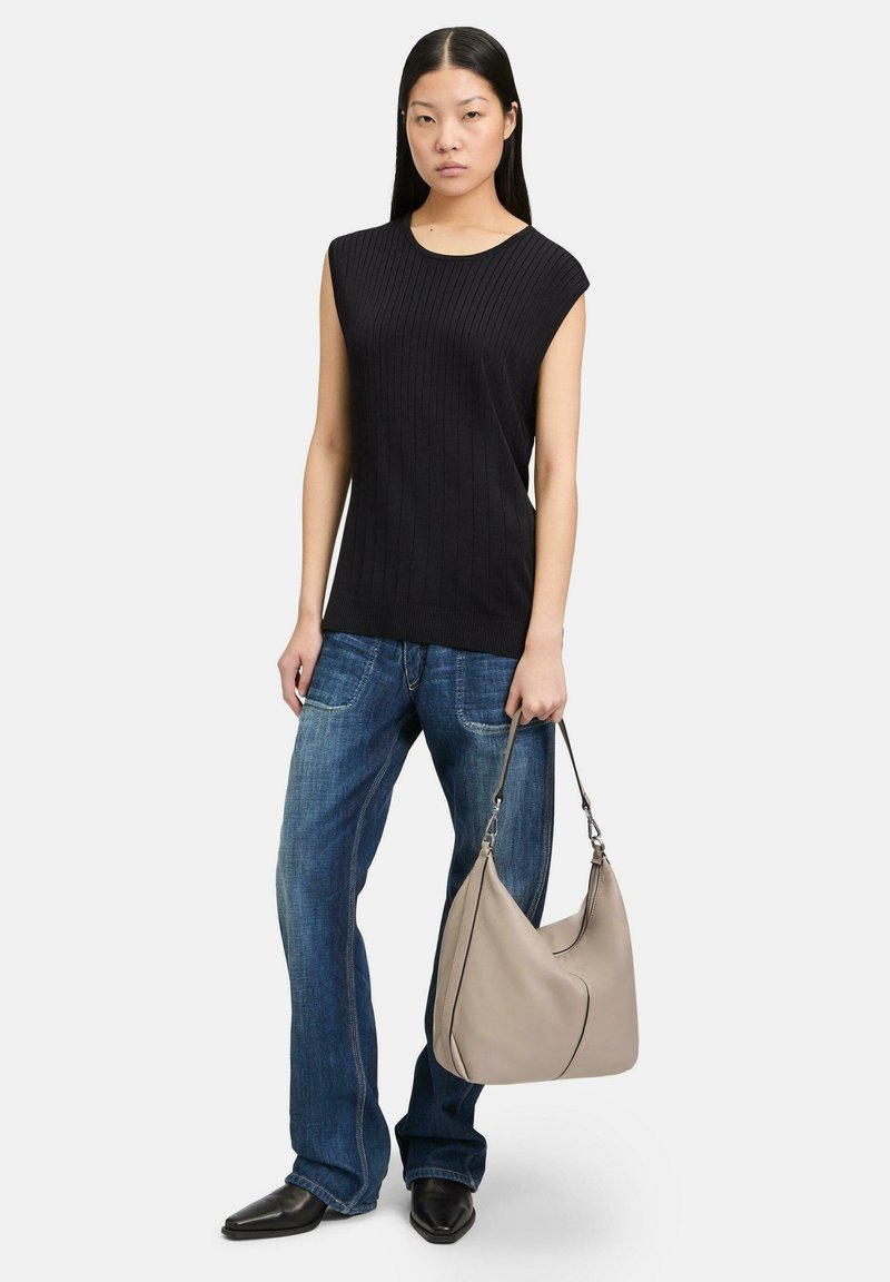 Czarna ribbed bezrękawnik, niebieskie jeansy o luźnym kroju i beżowa torba hobo z kontrastowym wykończeniem. Modelka w wyostrzałych czarnych butach.