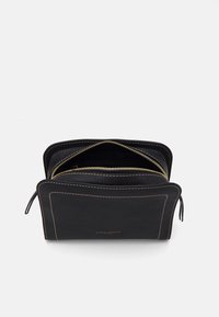Portafoglio in pelle nera con cuciture beige, scomparto con zip parzialmente aperto e nome del marchio in oro goffrato sul fronte.