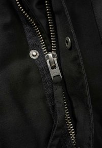 Černá bunda s výrazným stříbrným zipem s tahem na zip s logem, kovovými druky a texturovanou látkou.