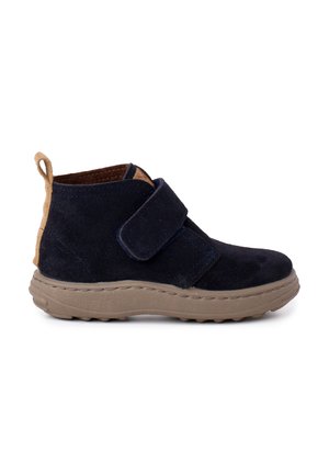 Stivaletti in suede blu navy con una fascia e un tab sul tallone beige, caratterizzati da una suola in gomma spessa con una superficie testurizzata per una migliore presa.