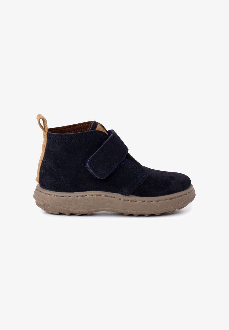 Bottes chelsea en suede bleu marine avec une sangle beige et une languette au talon, dotées d'une semelle en caoutchouc épaisse avec un motif texturé pour plus d'adhérence.