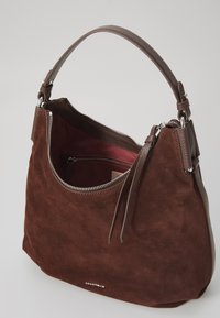 Braune Wildleder-Handtasche mit geschwungener Form, Lederakzenten und einem Reißverschluss. Das Innere verfügt über ein dunkleres Stofffutter und eine Reißverschlusstasche.