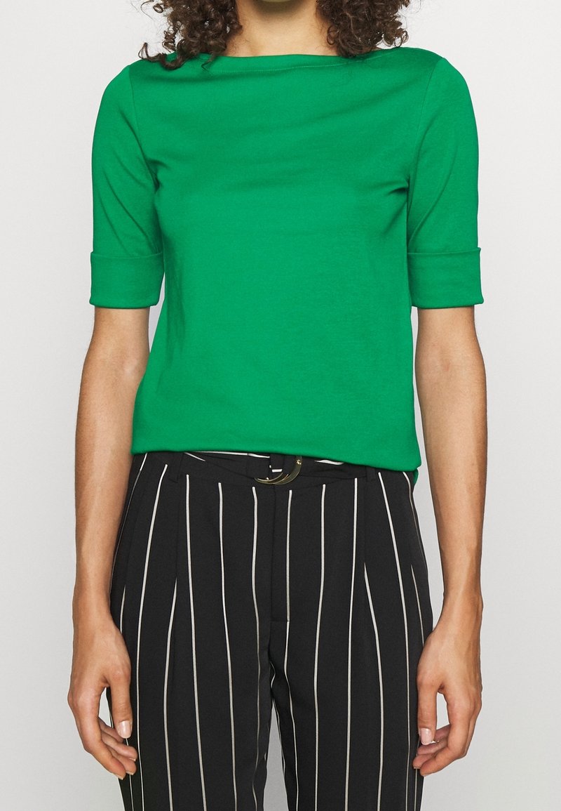 Grön kortärmad topp med rund halsringning, gjord av slätt tyg. Bärs med svarta och vita randiga byxor som har ett bälte.