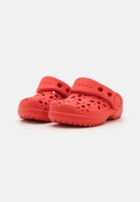 Punaiset puukengät, jotka on valmistettu kevyestä ja joustavasta materiaalista, joissa on tuuletusreiät ja takaosa, jossa on hihna turvallista istuvuutta varten. Pohja on kuvioitu pitävyyden takaamiseksi.