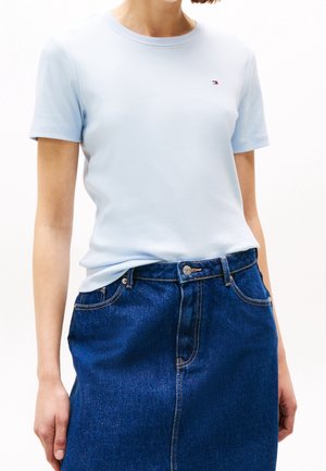 T-shirt bleu clair, manches courtes, col rond ; associé à une jupe en denim bleu foncé. Logo visible sur la poitrine gauche, coupe classique.