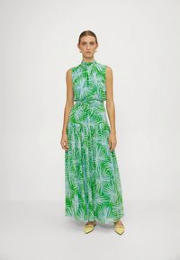 Vestido maxi com padrão de folhas verde e azul claro, design sem mangas, gola alta e cintura franzida, combinado com sapatos amarelos.