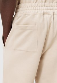 Beige sweatpants med elastisk talje og to sidelommer. Stoffet har en glat tekstur med en afslappet pasform og syninger langs sømmene.