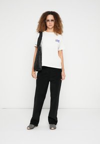 White short-sleeve t-shirt with blue and orange graphic, black wide-leg pants, gray shoes, and a black shoulder bag. Natural curly hair.