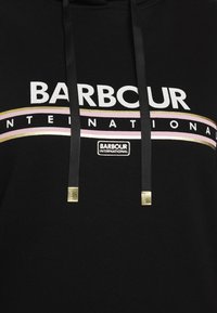 Černá mikina s kapucí a bílým nápisem "BARBOUR INTERNATIONAL." Obsahuje zlaté a růžové akcentní pruhy a zlaté šňůrky s konci.