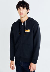 Sudadera con cremallera negra fabricada en una mezcla de algodón. Cuenta con capucha con cordones, bolsillo tipo canguro y logotipo naranja de "Levi's" en el pecho.