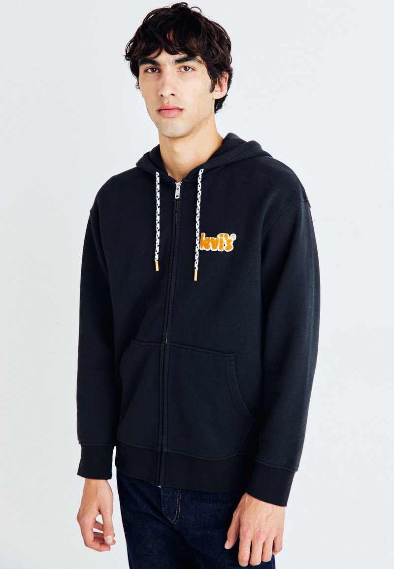 Sudadera con cremallera negra fabricada en una mezcla de algodón. Cuenta con capucha con cordones, bolsillo tipo canguro y logotipo naranja de "Levi's" en el pecho.