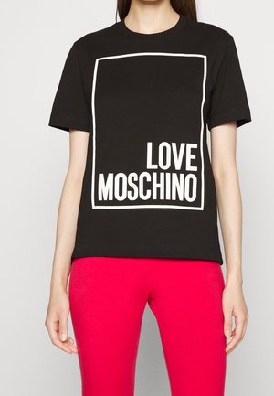 Personne portant un T-shirt noir avec un contour rectangulaire blanc et le texte « LOVE MOSCHINO », associé à un pantalon rouge vif.