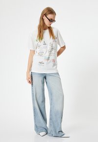 Hvid kortærmet t-shirt med farverige grafik og skitser; parret med lyseblå brede bukser og hvide spidse sko.