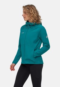 Giacca softshell teal con cappuccio, zip frontale, due tasche laterali e logo sul petto. Presenta un design aderente e un tessuto testurizzato.