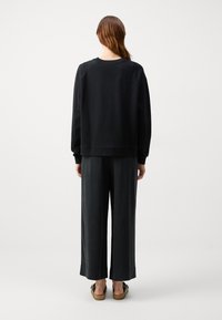 Sudadera negra con puños acanalados, combinada con pantalones oscuros de corte holgado. El conjunto presenta un diseño simple y minimalista.