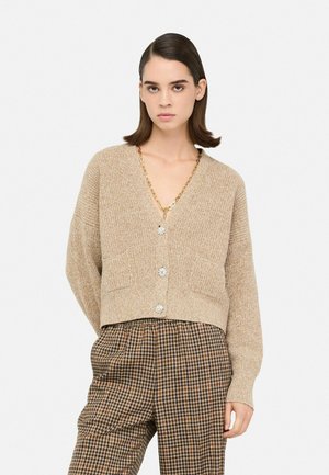 Cardigan lavorato a maglia beige con scollatura a V profonda, caratterizzato da tre bottoni decorativi e due tasche frontali, abbinato a pantaloni a quadri.
