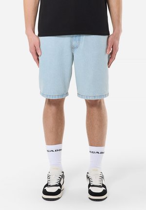 Shorts en jean bleu clair à coupe décontractée, ourlet retroussé et poches avant, assortis à des chaussettes blanches avec texte noir et des baskets noires.