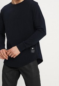 Námořnické tričko s dlouhým rukávem, kulatým výstřihem, vyrobené z měkké tkaniny. Obsahuje štítek na dolní straně, má zakřivený lem a úzké rukávy.