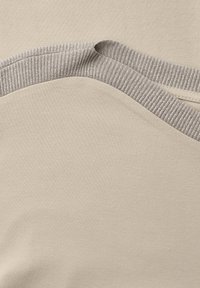 Tissu beige avec bordure en maille côtelée pliée, mettant en valeur le contraste de texture entre le tissu lisse et le bord côtelé.
