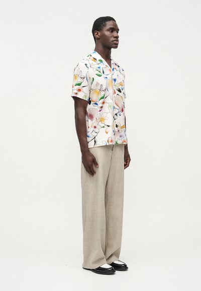 Κοντομάνικο πουκάμισο με λουλούδια σε απαλές αποχρώσεις, με γιακά με χαραγή. Συνδυάζεται με ανοιχτό μπεζ, άνετο παντελόνι και μαύρα παπούτσια.