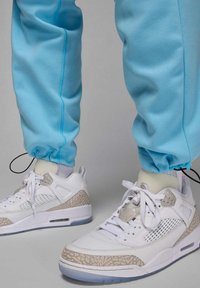 Białe sneakersy z szarymi wzorzystymi akcentami, wyposażone w siateczkowe panele, sznurowadła oraz przezroczystą podeszwę. Jasnoniebieskie spodnie dresowe z elastycznymi mankietami.