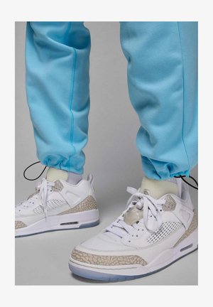 Białe sneakersy z szarymi wzorzystymi akcentami, wyposażone w siateczkowe panele, sznurowadła oraz przezroczystą podeszwę. Jasnoniebieskie spodnie dresowe z elastycznymi mankietami.