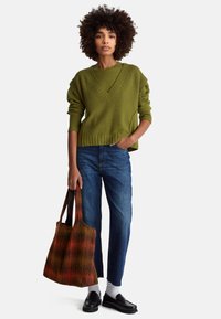 Olivově zelený žebrovaný svetr s výstřihem do V, kombinovaný s modrými džínami, bílými ponožkami, černými mokasíny a vícebarevnou pletenou taškou.
