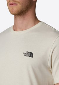 Krémové bavlněné tričko s kulatým výstřihem a krátkými rukávy. Na levé části hrudi má černé logo "The North Face."