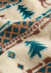 Koc polarowy o kremowym tle, z turkusowymi drzewami i brązowymi wzorami geometrycznymi. Tekstura jest miękka i puszysta, co zwiększa ciepło.